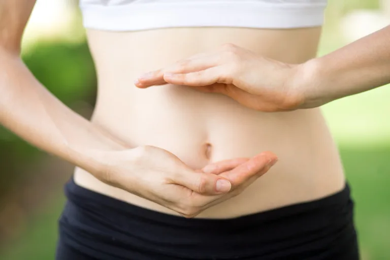 Gut-Friendly Foods: a woman's hands frame her bare stomach outdoors in a green garden