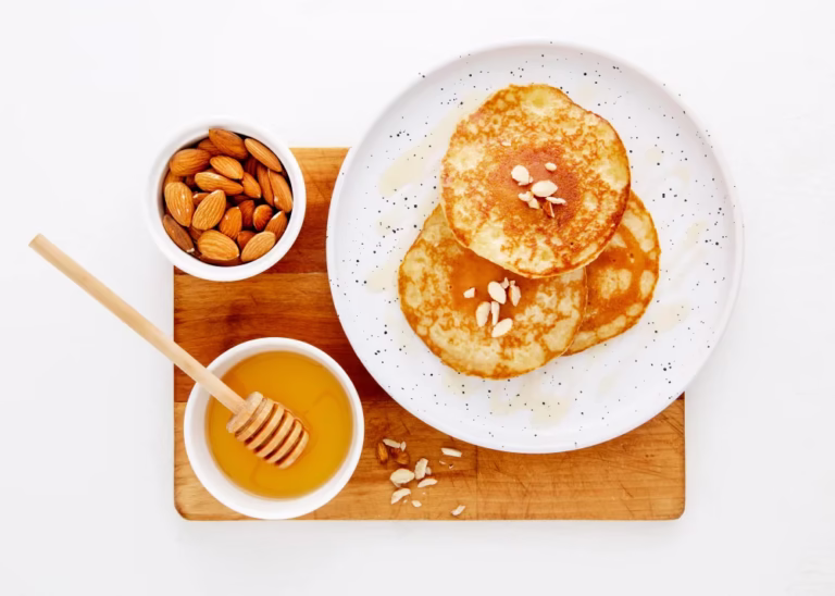 Almond Flour Pancakes: a stack of golden pancakes with honey, almonds and a honey dipper on a wooden board