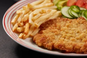 Air Fryer Magic: a crispy breaded chicken cutlet with fries, cucumber and tomato on a striped plate