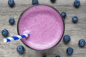 Blueberry smoothie in a glass with a blue-and-white striped straw, seen from above with fresh blueberries scattered around