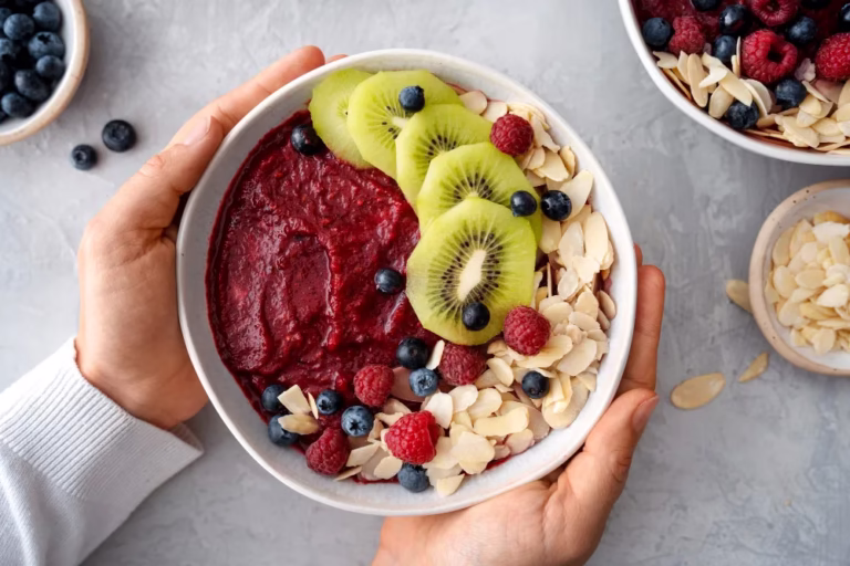 Healthy Smoothie Bowl Recipe: hands hold a berry smoothie bowl topped with kiwi, raspberries, blueberries and almond flakes