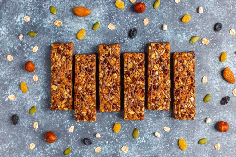 Homemade Energy Bars: six oat and nut bars lined up on a grey surface with scattered almonds, seeds and raisins