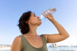 Hydration in Bariatric Dieting: a woman in a green tank top drinks from a water bottle under a blue sky