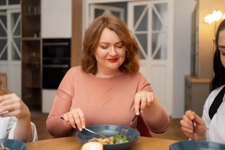 Mindful Eating After Bariatric Surgery: a woman eats slowly with knife and fork at a family table, eyes lowered to her plate