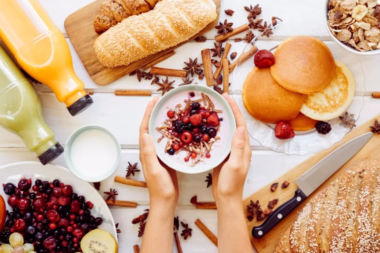 Diabetic Breakfast Ideas: hands hold a bowl of yogurt with berries above a table with bread, juice, milk and fresh fruit