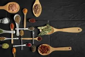 Herbs for Diabetes: wooden and metal spoons filled with ground spices, seeds, salt and dried herbs on black slate