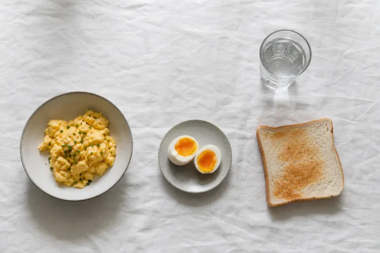 Soft scrambled eggs, a halved soft-boiled egg, plain white toast and a glass of water on white linen